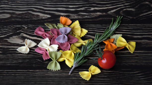 suchy kolorowy włoski makaron farfalle lub łuki z rozmarynem i pomidorem - bow tie pasta italian cuisine bow heap zdjęcia i obrazy z banku zdjęć