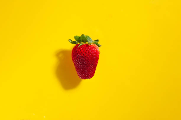 istock Single red ripe strawberry on yellow background with shadow 1217910992
