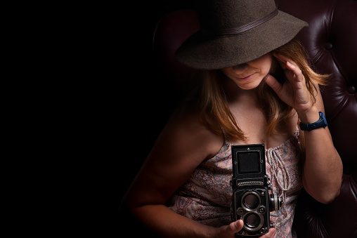 Pretty woman looking into antique camera wearing brown Fedora Hat with covering her eyes.