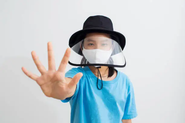 Vietnamese girls wearing hat with face shield and mask for protect and show stop hands gesture for stop corona virus outbreak.Wuhan coronavirus and epidemic virus symptoms.