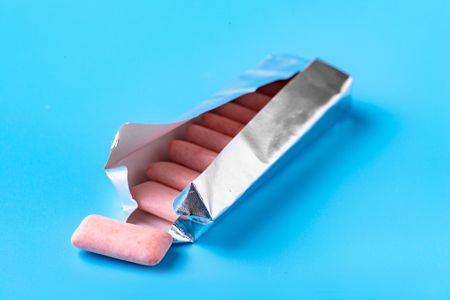 Pink chewing gum drops out of the package. Blue background. Beautiful photo
