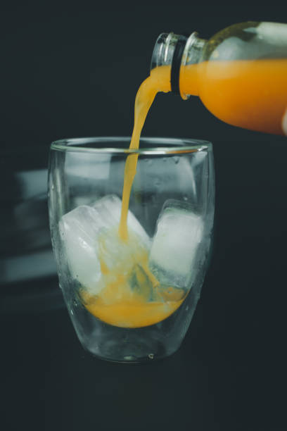 istock Pouring orange juice on a glass on black background 1217921030