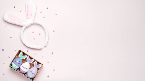 istock Funny kawaii bunny eggs and bunny rabbit ears for kids on pastel pink table top, Easter holiday concept. Easter decoration and set for creative activity for kids with crayons and notebook flat lay 1217921105