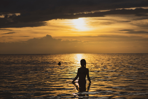 Silhouette of a 19-year-old woman walking in the sea at sunset.  Location: Ko Phangan, Thailand