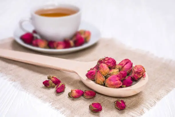 Herbal tea with rosebuds. White cup with hot tea. A wooden spoon with dried flower buds on a linen napkin.