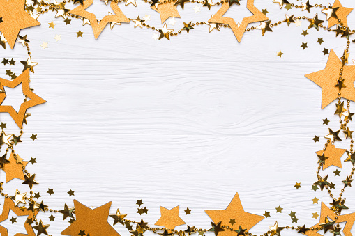 Flat lay frame of big and small stars of confetti. Golden beads of shine stars. Festive decor on a white wooden background. View from above.