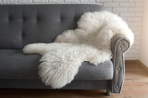 White sheep skin on a gray sofa. A cozy place to relax in the apartment. Modern Scandinavian style interior