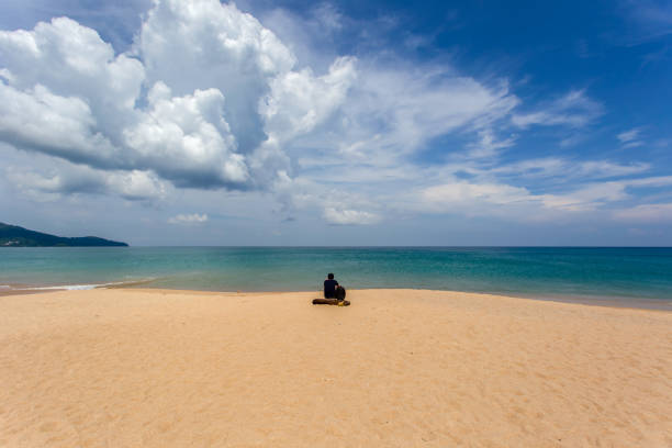 istock Young man sitting on the beach at Mai Khao Beach 1217923200