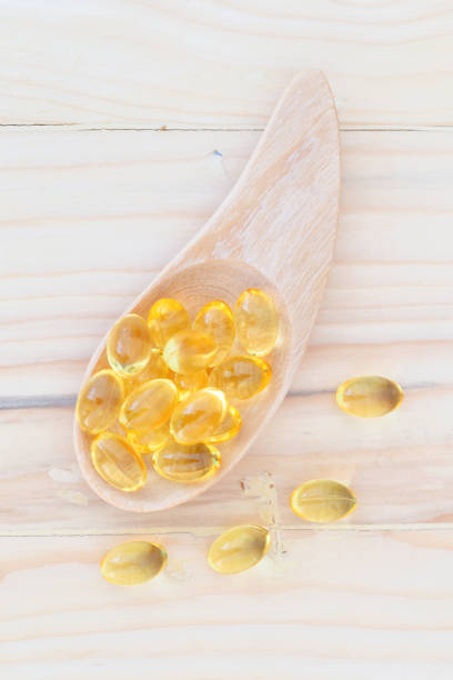 капсулы рыбьего жира с омега-3 и витамином d на ложке дерева с деревянным фоном, концепция здорового питания. - fish oil cod liver oil capsule pill стоковые фото и изображения