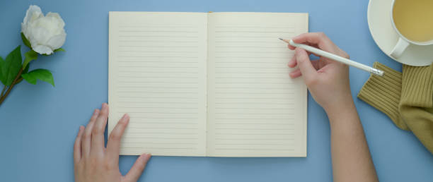 istock Overhead shot of female university student doing homework on blank notebook on light blue table 1217931586
