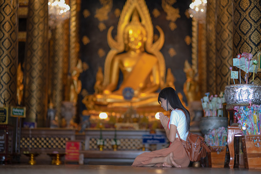 Woman traveller pay gentle respect to the buddha statue in the temple, praying respect for a better life forward