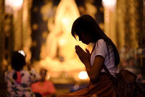 silhouette of woman traveller pay gentle respect to the buddha statue in the temple, praying respect for a better life forward
