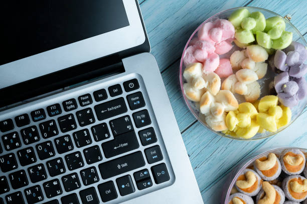 Close up of a hand using laptop computer while sitting at the kitchen table, eating cookies while working at home during lock down because corona virus
