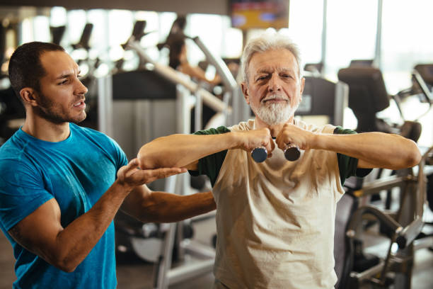 istock Senior man exercising with personal trainer using dumbbells at the gym 1217952288