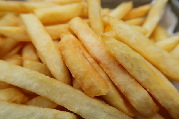 Stock photo of crispy chunky chips / French fries takeaway food at bar restaurant, unhealthy greasy snack food fried in peanut vegetable oil, served in metal basket, English takeaway chips ready to eat with salt and vinegar imagen de patatas fritas crujientes / papas fritas comida para llevar en el bar restaurante, bocadillos grasosas poco saludables fritos en aceite de verduras de maní, servidos en cesta de metal, patatas fritas inglesas listas para comer con sal y vinagre