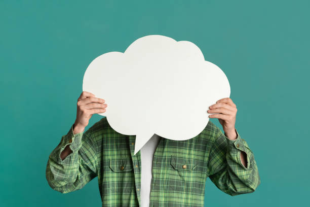 istock Millennial guy covering his face with speech bubble on turquoise background, space for design 1217959010