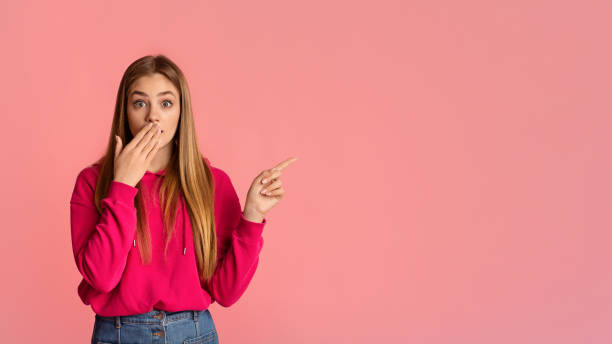 istock Girl closed mouth with hand and points finger 1217959687