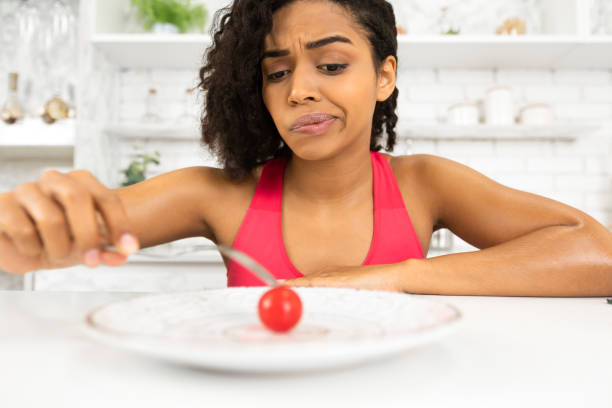 istock Depressed afro lady looking at tiny tomato on a plate 1217960565