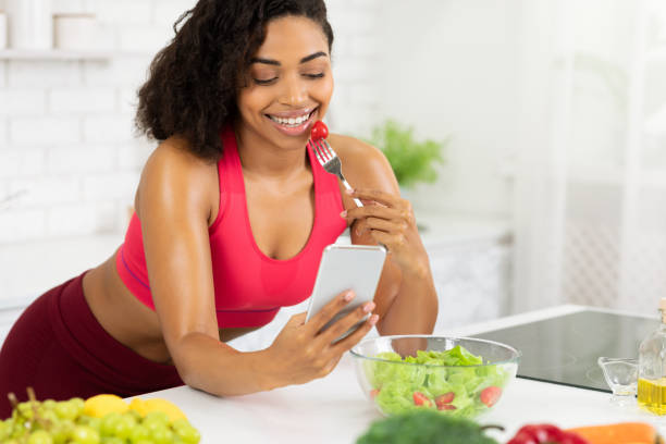 istock Black girl using smartphone and eating vegetable salad 1217960601