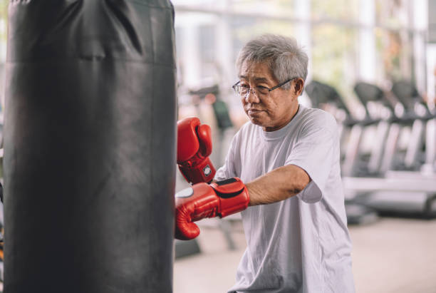 asian chinese senior citizen boxer training with puching bag in gym doing exercise in gym old man boxing stock pictures, royalty-free photos & images
