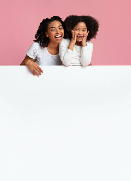 istock Overjoyed Black Mom And Little Daughter Leaning On White Advertisement Board 1217961004