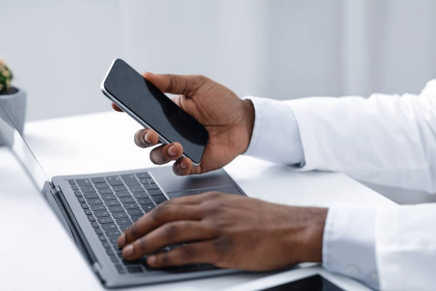 istock Close up of doc hands holding phone and using laptop 1217961141