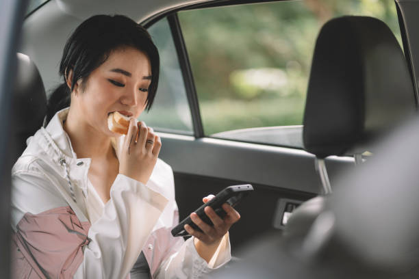 istock young asian chinese woman eating inside a car while using phone 1217962241