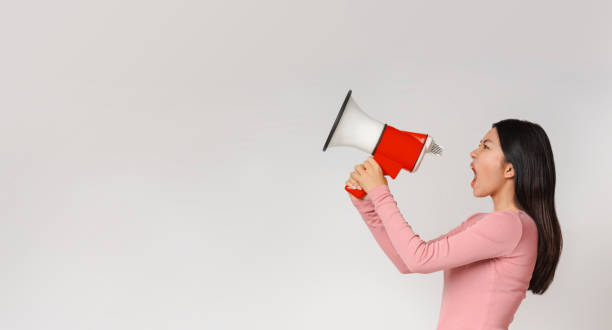 istock Angry asian woman shouting in megaphone over grey background 1217962285