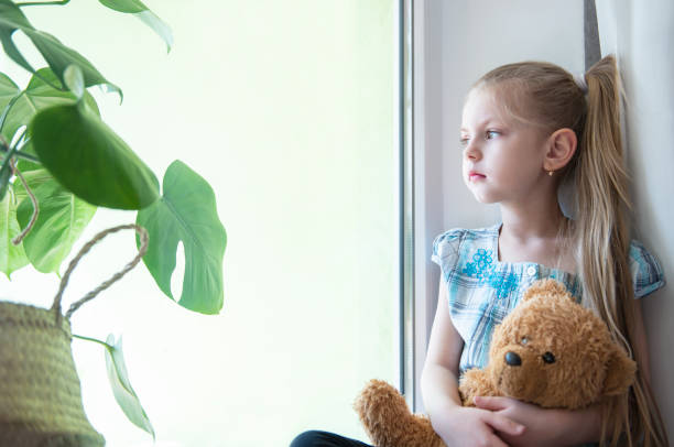 istock Sad child girl by the window 1217962763