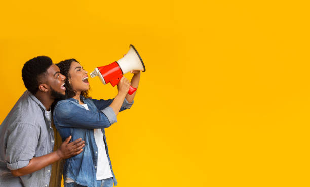 istock Making announcement. Positive black couple shouting in megaphone at copy space 1217962833