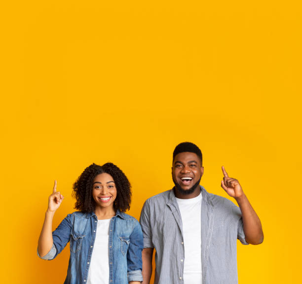 istock Joyful black couple pointing upwards at copy space and smiling 1217962914