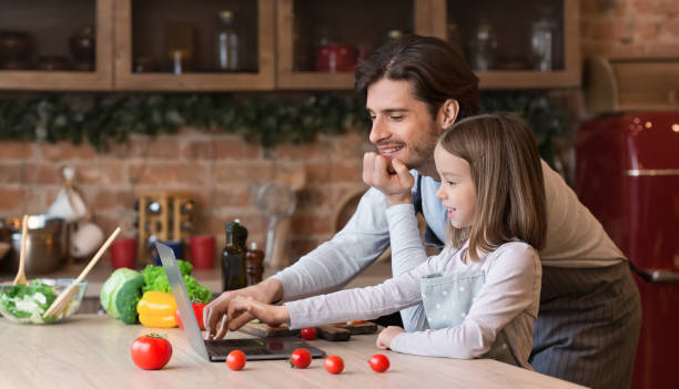 istock Young dad and his daughter reading recipe on laptop in kitchen 1217963699
