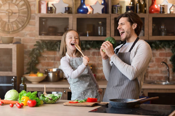 istock Father and daughter having fun while preparing lunch in kitchen, singing 1217963715