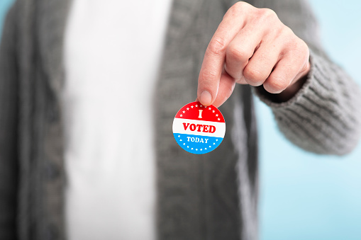 Hand of man holding an I voted today sticker with American Flag, blurred background
