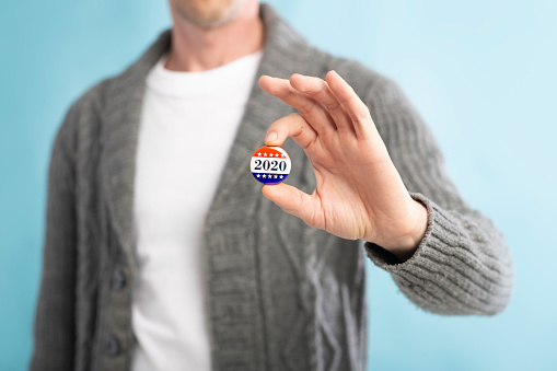 American democracy elections. Unrecognizable american citizen holding voting pin on blurred blue background