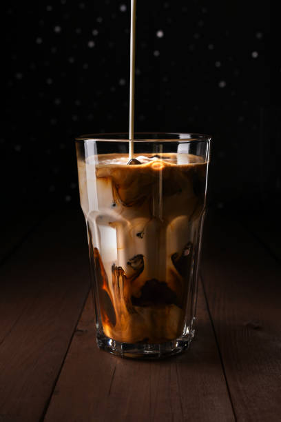 istock Ice coffee on a wood table with cream pouring into glass. 1217965431