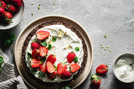 Top view of freshly prepared yogurt strawberry pie on gray surface. Sweet pie made of yogurt and garnished with strawberries and pistachio in kitchen.