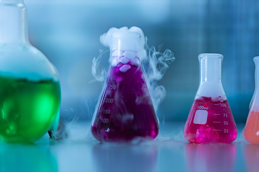 Close up of group of beakers with chemical reactions in laboratory. Copy space. Focus is on beaker with pink liquid.