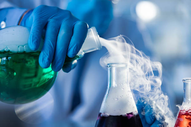Close up of unrecognizable scientist pouring smoke from a beaker with green liquid in laboratory.