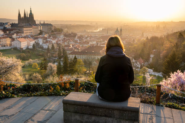 Lonely woman in 40s relaxing outside in city park and enjoying the view of Prague. Female sitting on a bench, looking at beautiful sunrise over old town Lonely woman in 40s relaxing outside in city park and enjoying the view of Prague. Female sitting on a bench, looking at beautiful sunrise over old town. prague skyline panoramic scenics stock pictures, royalty-free photos & images