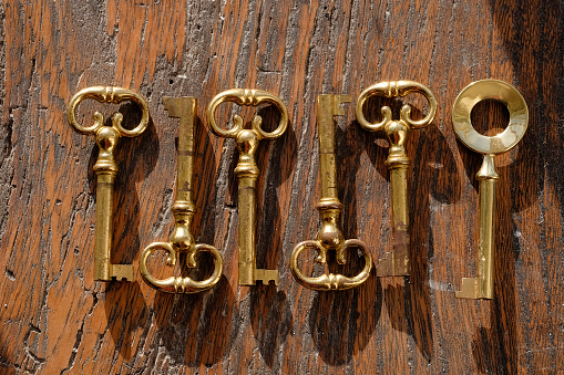 six ornate brass keys in a row on a wooden background