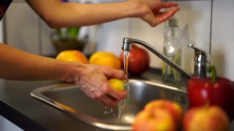 Woman washing fruits under running water in kitchen sink