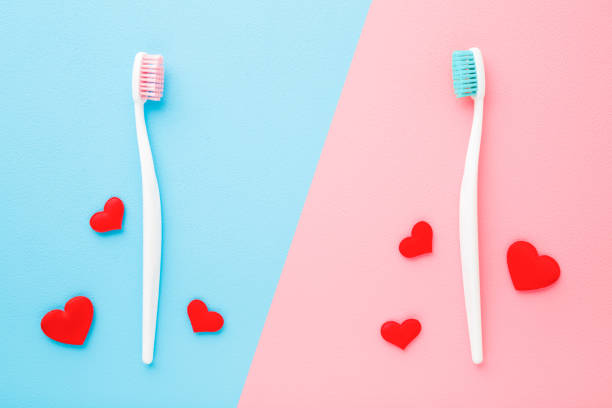 istock Two white toothbrushes with bright red hearts. Blue pink table background. Pastel colors. Man and woman teeth hygiene. Living together. Love concept. Closeup. Top down view. Flat lay. 1217986086