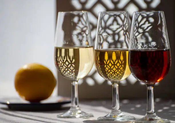 Glasses with cold dry fino and sweet cream sherry fortified wine in summer sunlights, andalusian style interior on background