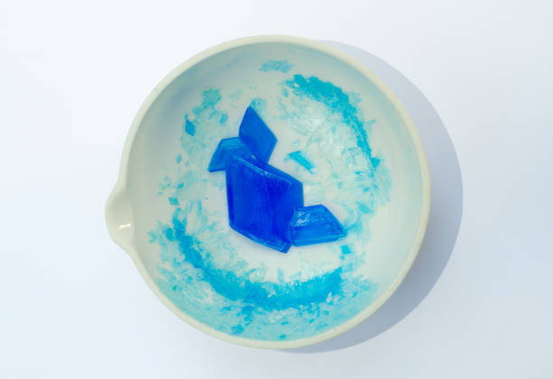 A white porcelain evaporating basin containing large blue copper sulphate crystals isolated on a white background.The crystals were produced by reacting copper oxide powder with sulphuric acid, filtration, and then slow evaporation.