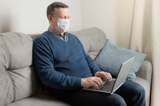 Photo of Adult man in protective mask work at home by laptop. Remote work. Covid-19. Quarantine. Stay at home.