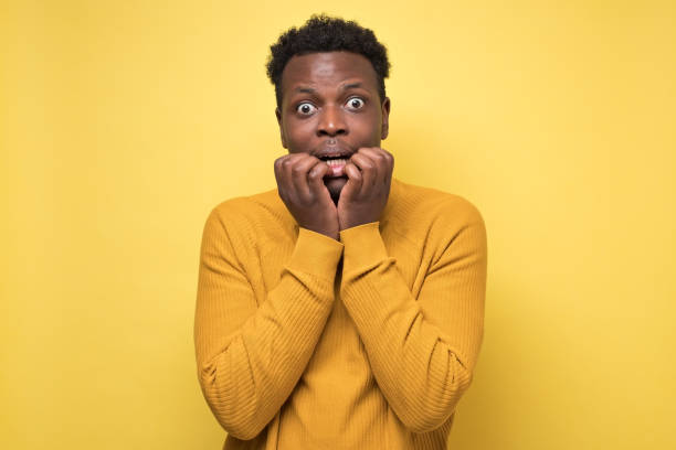 African scared guy biting nails, gawp at camera see something terrible African scared guy biting nails, gawp at camera see something terrible, sensitive cowardly man watching thriller. Mental problem during quarantine. Scared to be alone. gawp stock pictures, royalty-free photos & images