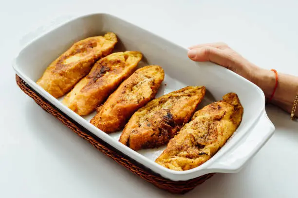 Photo of Female hand holding a tray with torrijas, a typical Spanish sweet fried toasts of sliced bread soaked in eggs and milk, on white background