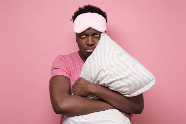istock Sad african american man with mask and pillow being stressed staying alone 1217997501