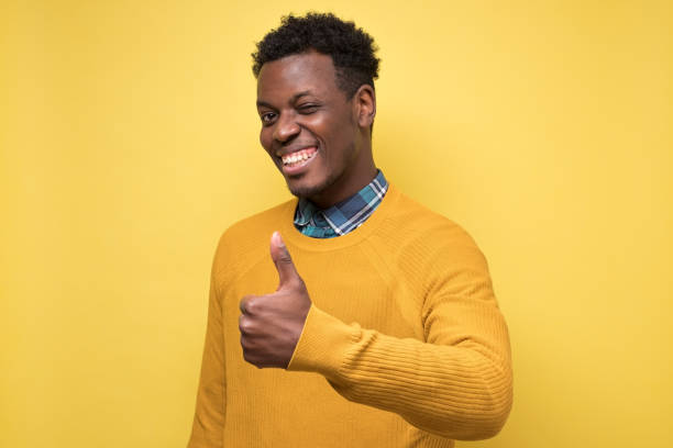istock man with cheerful attitude showing thumb up on yellow wall. 1217997561